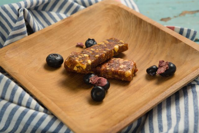 Granola bars with blueberries on a wooden plate, perfect for promoting healthy eating, breakfast ideas, or snack options. Ideal for use in food blogs, nutrition articles, or advertisements for organic and natural food products.