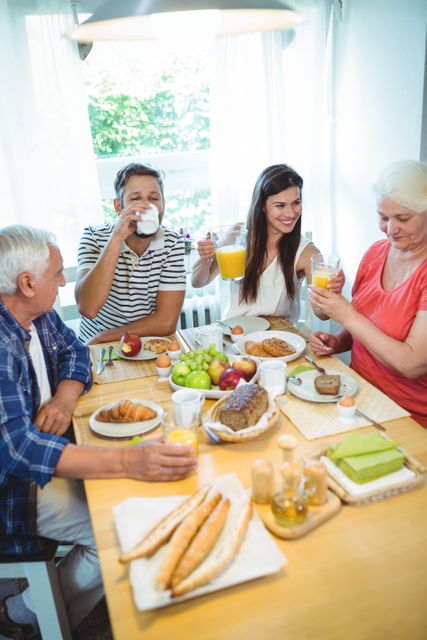 Family members sitting around a table, sharing a hearty breakfast at home. The scene is lively and filled with joy as they enjoy fresh fruits, pastries, and beverages. This can be used for content about family bonding, morning routines, healthy eating, and home life.