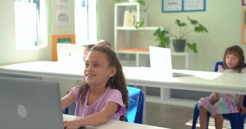 Smiling African American teen using laptop in sunlit classroom learning with classmates