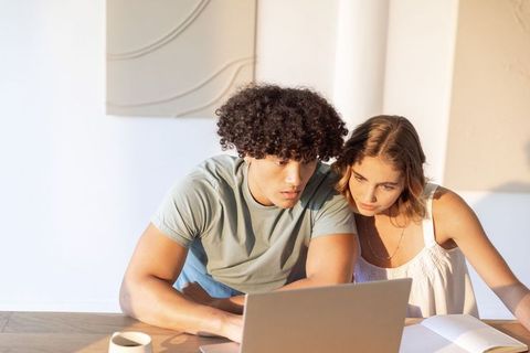 Young couple collaborating on laptop at sunlit wooden table planning finances and study