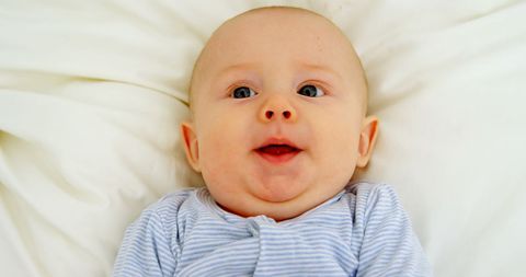 Smiling Baby Relaxing on Soft White Bed
