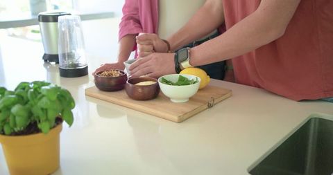 Couple preparing fresh pesto ingredients on cutting board in bright home kitchen