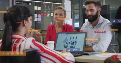 Team collaborating over laptop with data charts while leader presenting in glass conference room