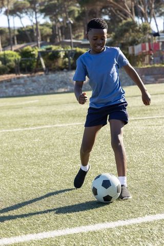 African american boy dribbling soccer ball on sunny turf field for youth sports