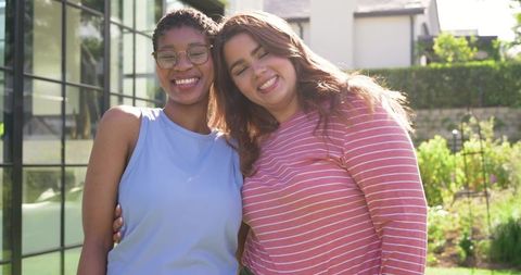 Smiling african american women friends leaning together in sunny backyard garden