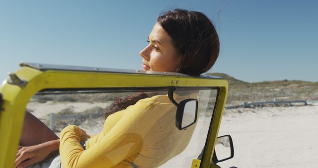 Woman in yellow shirt is enjoying her time in a convertible jeep on a sunny beach. Her relaxed demeanor captures a carefree and adventurous spirit. Ideal for advertising vacation packages, car rentals, or lifestyle articles about travel and leisure.