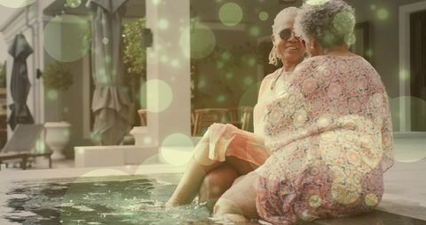 Senior women chatting poolside dipping feet in water enjoying sunny friendship