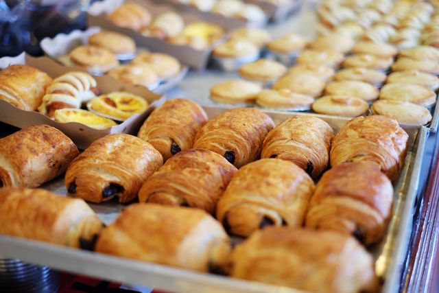 Freshly baked pastries including chocolate croissants and egg custard tarts are displayed in bakery. Ideal for use in food blogs, culinary magazines, advertisement for bakeries, and menu designs to showcase delicious baked goods.
