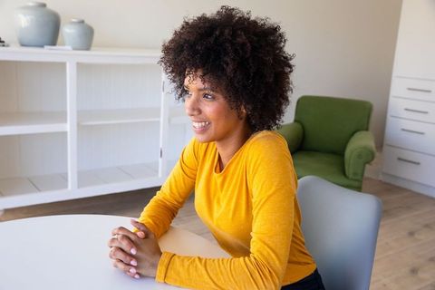 Smiling woman in mustard yellow top seated at home