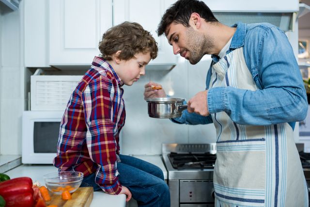 Father and son cooking together in kitchen, showcasing family bonding and togetherness. Ideal for use in parenting blogs, family-oriented advertisements, cooking tutorials, and lifestyle articles focusing on family activities and home life.