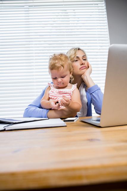 Stressed mother with baby girl using laptop at home