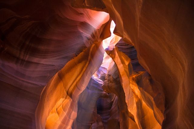 Slot canyon with stunning rock formations featuring layers of orange, purple, and pink sandstone. Sunlight filters through the narrow openings, creating striking beams and shadows. Ideal for illustrating geological wonders, natural beauty, or travel destinations in the American Southwest.