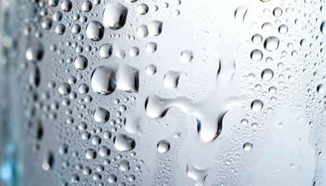 Macro condensation on glass with water droplets, rivulets, bokeh reflections, cool cyan highlights