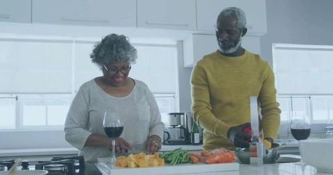 Senior couple preparing healthy meal with wine and fresh vegetables in modern kitchen