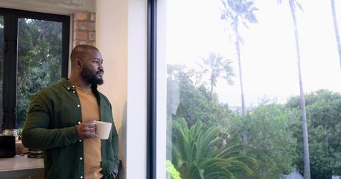 Mid-30s African American man enjoying morning coffee while gazing out large window