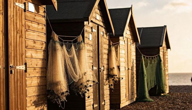 Golden sunset beach huts lining pebbled shore with weathered fishing nets and coastal cabins