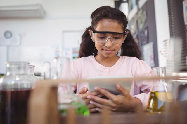 Young girl in a science laboratory using a digital tablet while wearing safety goggles. Ideal for educational materials, technology in education, STEM programs, and school science projects.