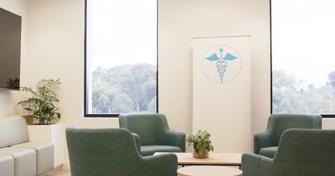 Welcoming clinic waiting area featuring green armchairs, round tables and daylight