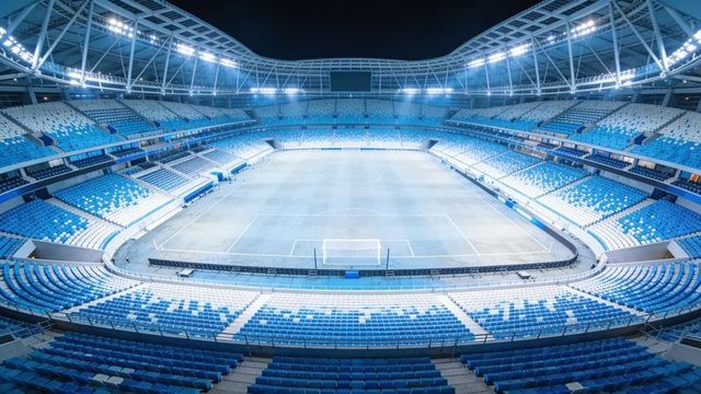 Illuminating empty modern football stadium at night with blue seats and floodlit pitch