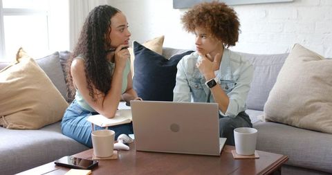 African American women collaborating on project with laptop and notebooks on couch