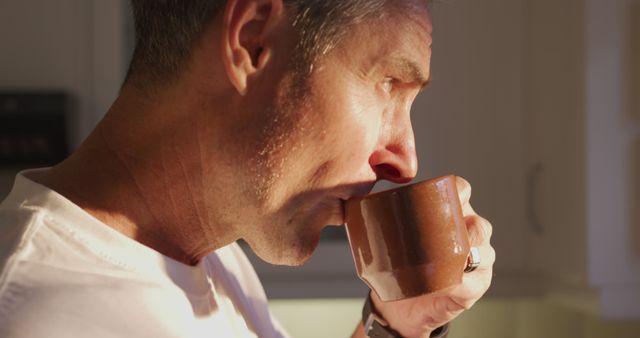 Man drinking coffee in kitchen during morning relaxation. Suitable for health, lifestyle, morning routine, and relaxation themes.