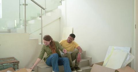Couple unpacking art and moving boxes on sunlit modern staircase