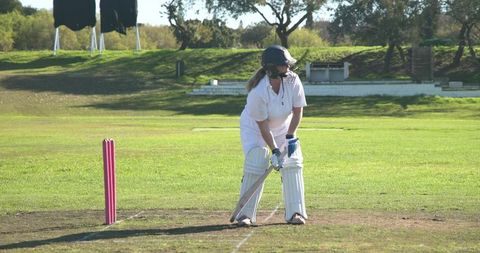 Female Cricketer Bats on Grass Pitch in Protective Gear