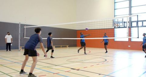 High school boys playing indoor volleyball, spiking ball over net in bright gymnasium action