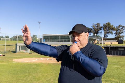 Baseball coach blowing whistle and signaling on sunny diamond during game
