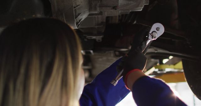 Female mechanic working under a car with a wrench in an auto repair shop, demonstrating professional car maintenance. Ideal for content related to vehicle repair, women in trades, mechanical work, and automotive services.
