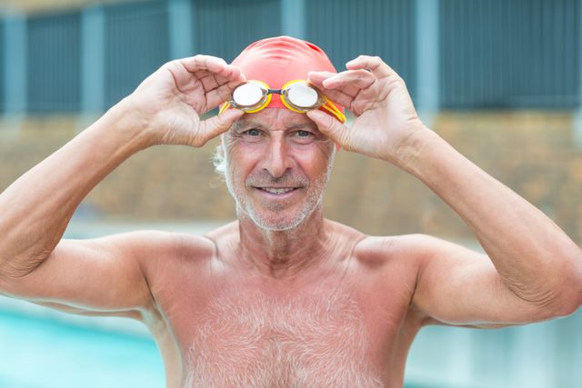 Portrait of senior man holding swimming goggles at poolside 