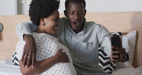 Expectant Couple Taking Selfie on Bed with Joy