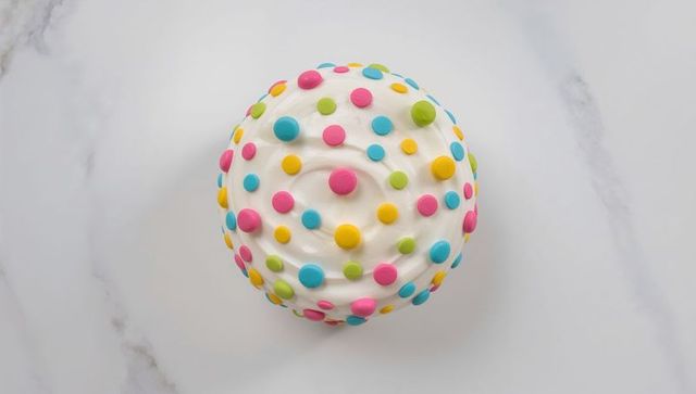 Playful confetti cupcake with white swirl frosting on clean marble surface for bakery