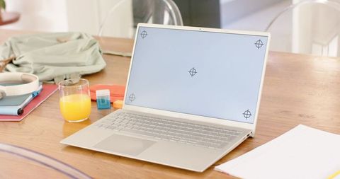 Minimal workspace featuring open silver laptop, orange juice, headphones on wooden table