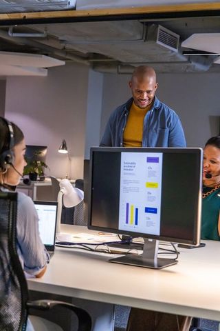Collaborating diverse team reviewing infographic on desktop monitor in open-plan office