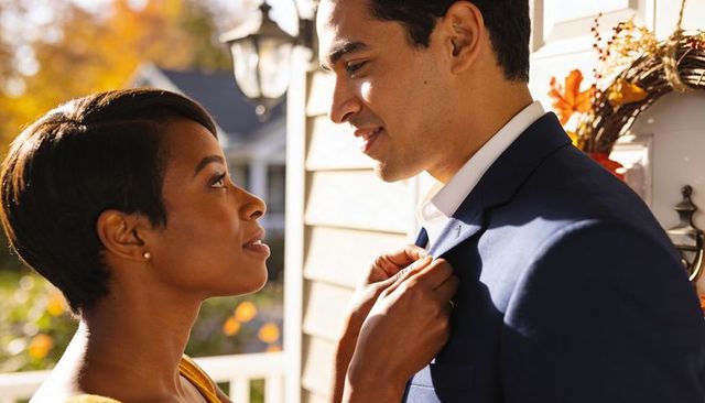Couple sharing tender moment while woman pins boutonniere on partner in autumn doorway