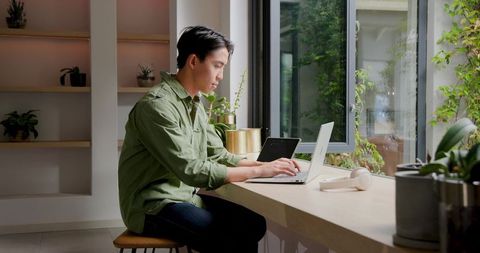 Man Working on Laptop at Modern Home Workspace by Window