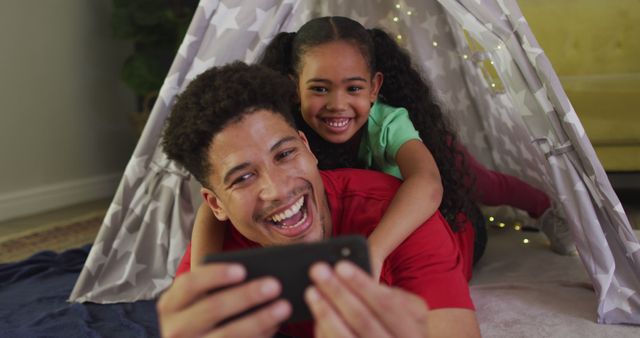 Happy biracial father and daughter using smartphone together. domestic lifestyle, spending free time at home.