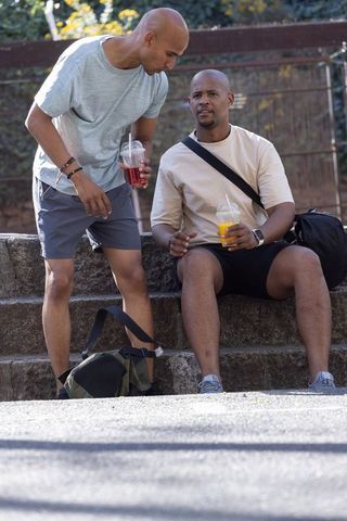 Two african american men chatting on stone steps in casual sportswear holding cold drinks