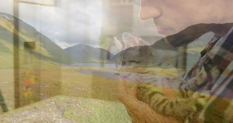 Double-exposure man holding tabby kitten with reflective window over loch and glen, plaid shirt