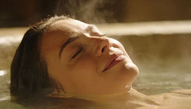 Woman relaxing in steaming spa tub closeup, floating face and bare shoulders, serene expression