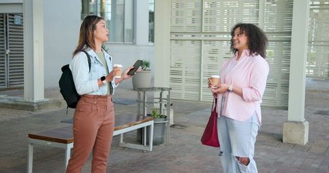 Asian and african american women chatting on campus with coffee casual outdoor friendship