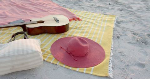 Guitar and Pink Sun Hat on Sandy Beach Blanket Afternoon