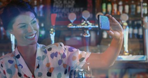 Woman Enjoying Video Call at Bar Under Vibrant Lights