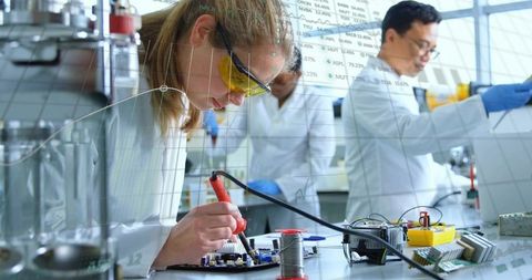 Laboratory engineer soldering prototype circuit on bench while team testing electronics components