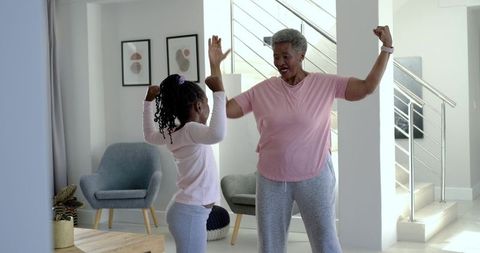 Senior woman and granddaughter flexing arms celebrating joyful bond in bright living room