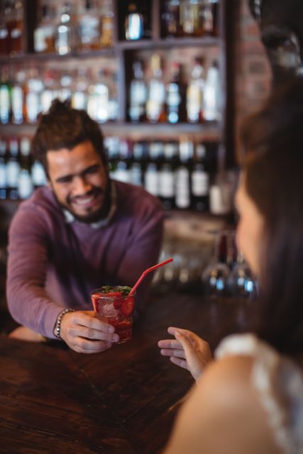 Male bartender serving a cocktail drink to customer at bar counter