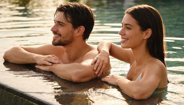 Sunset pool romance: smiling young couple leaning on stone coping, golden hour glow