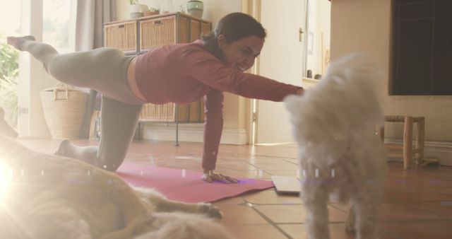 A woman is doing yoga or an exercise routine inside her living room, reaching out towards a small dog while stretching on a pink yoga mat. This image portrays a healthy and active lifestyle, as well as a cozy home environment with the fond presence of a pet. It can be used for promoting home workout routines, pet-friendly spaces, healthy living campaigns, or fitness blogs.