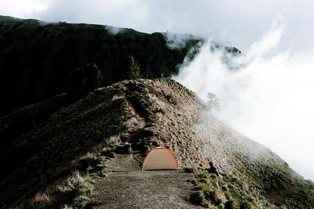 Tent standing alone on a mountain peak surrounded by misty clouds and rugged landscapes. Ideal for travel and adventure themes, inspiring trekking experiences, promoting outdoor activities and solitude. Perfect for nature-focused websites and hiking gear advertisements.